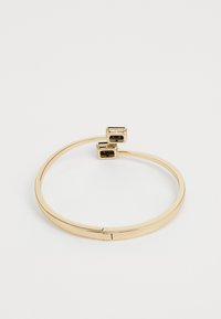 Pulsera abierta de bangle de oro con dos gemas negras rectangulares en cada extremo, sobre un fondo blanco liso.