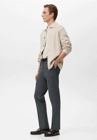 Beżowy sweter na guziki z kołnierzem, szare spodnie i ciemne buty. Sweter zapinany na guziki; spodnie o kroju dopasowanym.