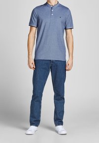 Blue short-sleeve polo shirt with a buttoned collar, featuring a small logo, paired with blue denim jeans and white sneakers.