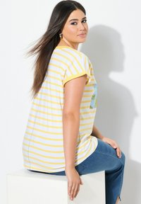 Kelta-valkoraidallinen t-paita lyhyillä hihoilla, jossa on edessä sininen grafiikka, yhdistettynä sinisiin farkkuihin.