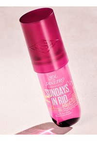 Różowa cylindryczna butelka perfum z przezroczystą nakrętką. Posiada etykietę "Sundays in Rio" oraz dekoracyjne akcenty. Błyszczące wykończenie, smukły design.