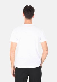 T-shirt bianco in cotone con una vestibilità classica, maniche corte e scollatura a girocollo, visto di spalle, indossato con pantaloni neri.
