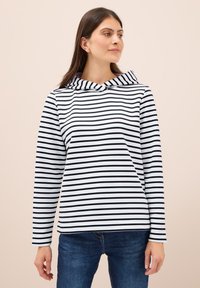 Sudadera a rayas blancas y negras con cuello doblado y mangas largas, hecha de una tela suave; llevada con jeans de mezclilla azules.