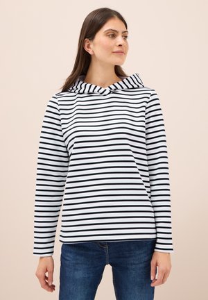 Haut à capuche rayé noir et blanc avec un col rabattu et des manches longues, fabriqué en tissu doux ; porté avec un jean en denim bleu.