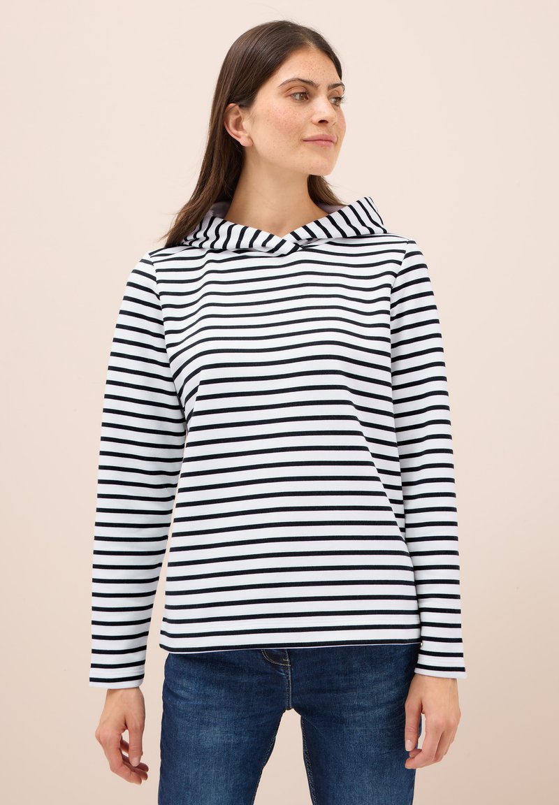 Sudadera a rayas blancas y negras con cuello doblado y mangas largas, hecha de una tela suave; llevada con jeans de mezclilla azules.