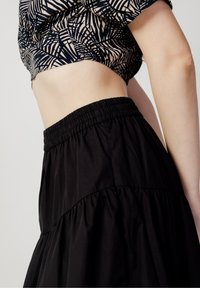 Schwarzer schichtweise Rock mit glatter Textur und elastischem Bund, kombiniert mit einem kurz geschnittenen Oberteil mit einem geometrischen Palmblätter-Druck.