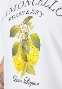 Camiseta blanca con un gráfico de limón con hojas verdes y flores blancas, adornada con strass. El texto dice "Limoncello Fresco y Jugoso."