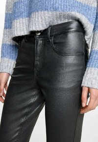 Musta tekonahkahaalari, jossa on tyylikäs pinta ja hillitty kiilto. Yhdistetty harmaansiniseen raidalliseen neulepaitaan.