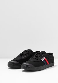 Black canvas sneakers with a rubber toe cap and patterned sole. Features red and blue stripes on the side and black laces.
