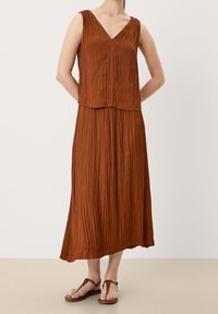 Brown pleated dress with a V-neck, sleeveless design, flowing silhouette, and lightweight texture; paired with brown flat sandals.