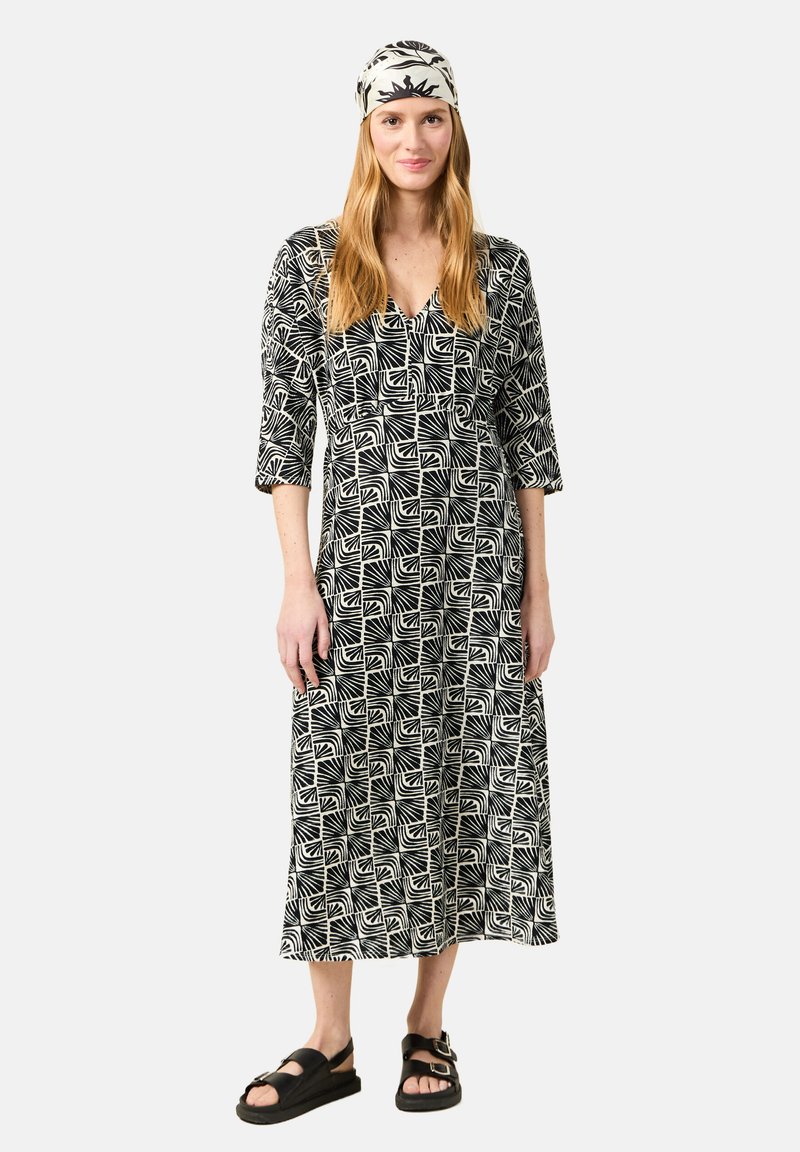 Schwarz-weiß gemustertes Kleid mit Dreiviertelärmeln, V-Ausschnitt und Knöchellänge. Kombiniert mit einem passenden Kopfband und Sandalen.