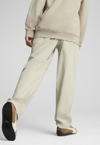 Felpa beige con polsini e orlo a coste. Pantaloni beige chiaro dal taglio morbido e comodo. Sneakers marroni e bianche con suola nera.