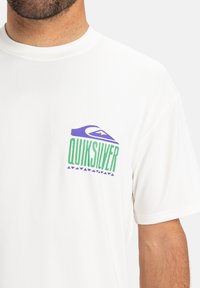 Camiseta de manga corta blanca con el logo multicolor de "Quiksilver" que presenta un diseño de ola y montaña, fabricada con una tela suave.