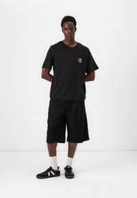 Black short-sleeve t-shirt with a small sun graphic on the chest, paired with black knee-length shorts and black sneakers with white accents.
