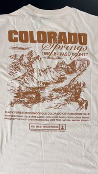 Bela bombažna majica s rjavim grafičnim tiskom gora, jezera in besedilom "COLORADO Springs 1990 - EL PASO COUNTY" z lokacijskimi podrobnostmi.