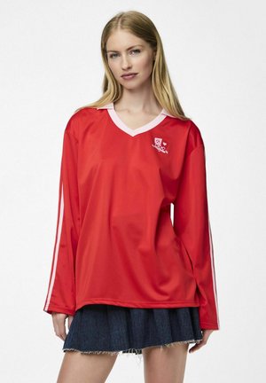 Rode sportshirt met lange mouwen en een V-hals, witte kraag en witte zijstrepen; beschikt over een logo op de borst. Glad textuur.