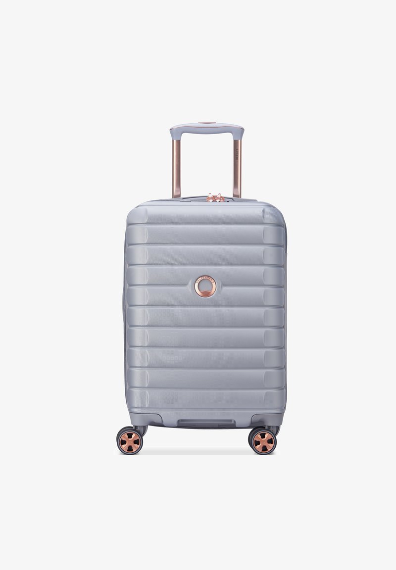 Valise rigide gris clair avec un design à côtes verticales, matériel en rose gold, une poignée télescopique et quatre roues pivotantes.