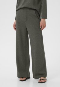 Pantaloni grigi a gamba larga realizzati in un tessuto morbido e testurizzato, con tasche laterali e una vestibilità rilassata, abbinati a sandali neri.