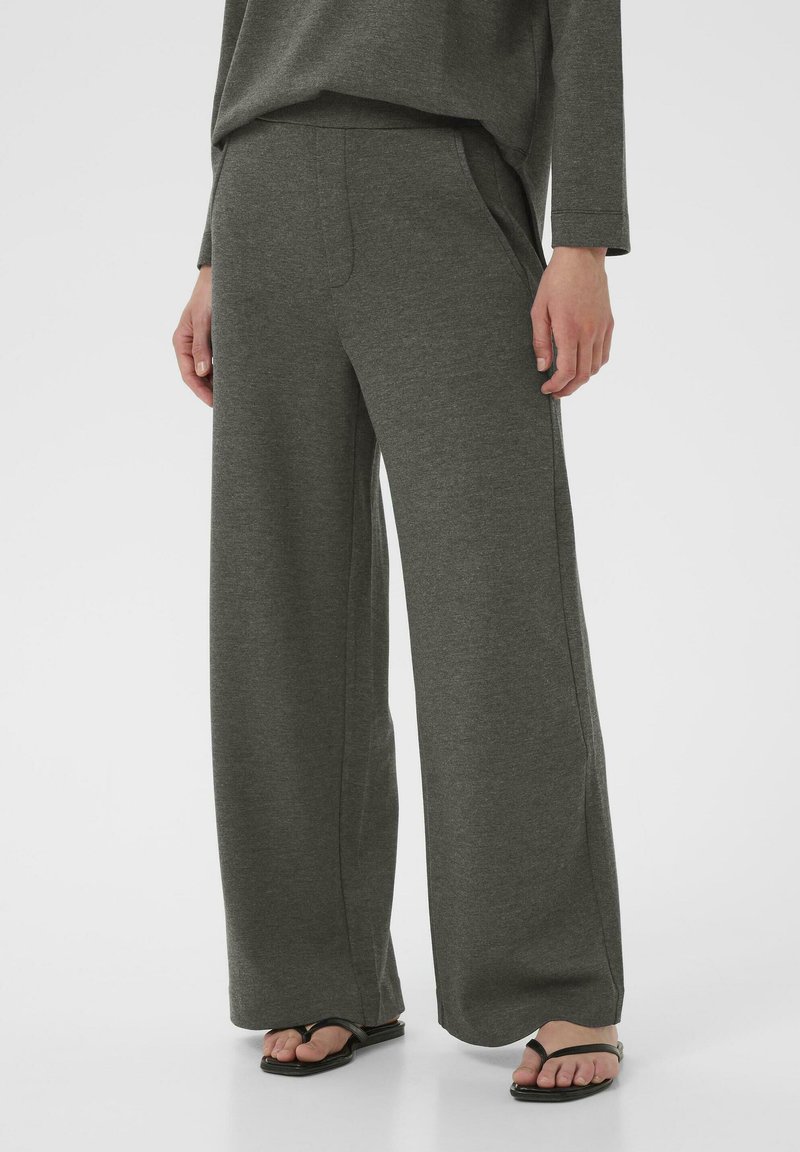 Pantaloni grigi a gamba larga realizzati in un tessuto morbido e testurizzato, con tasche laterali e una vestibilità rilassata, abbinati a sandali neri.