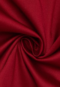 Tessuto rosso intenso, texture liscia, tessuto con una leggera lucentezza. Il materiale ha una leggera elasticità, raccolto a spirale per mostrare le complessità del design.