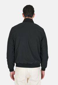 Giacca bomber nera con una texture liscia, polsini e orlo a coste, dotata di un colletto classico e una silhouette pulita.