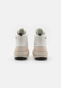 Bottes imperméables blanches et beiges avec une tige texturée, un col rembourré et une semelle texturée noire. Présente le logo Columbia sur le côté.