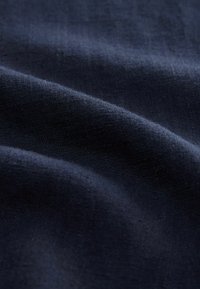 Tumedat navy-sinine kangas, millel on veidi tekstureeritud pind, pehmelt kortsud ja kergelt sädelev välimus. Materjal näib sile ja peenelt kootud.