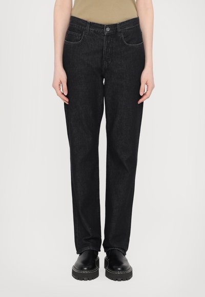 Jeans de denim negro con corte recto, cinco bolsillos y detalles de costura en contraste. Combinados con unos zapatos negros gruesos.