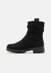 Bottines noires en matériau doux avec un design flou, bout rond et semelle en caoutchouc solide avec un motif texturé.
