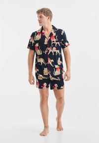 Granatowy zestaw piżam wykonany z bawełny, z nadrukiem w leopardzie z czerwonymi akcentami. Koszulka zapinana na guzik z krótkim rękawem oraz dopasowane szorty, gładka tekstura.