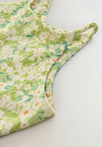 Top tanki, yang terbuat dari kain dengan pola floral yang menampilkan warna hijau dan krim, dengan aksen biru dan oranye. Tekstur lembut dan desain tanpa lengan.