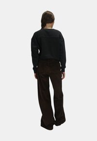 Felpa nera con spalle scese abbinata a pantaloni brown in corduroy a gamba larga, vista da dietro. Texture liscia, design casual.