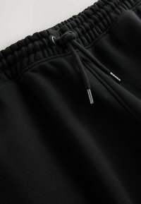 Pantalones de chándal negros de algodón con cinturilla elástica y cordón ajustable. Textura suave con detalles de costura sutil y ojales de ventilación.