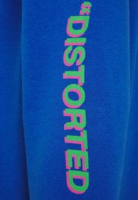Tessuto blu con testo verticale "DISTORTED" in lettere verdi contornate di rosa.