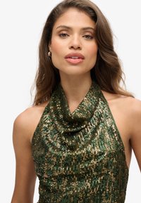 Groene pailletten haltertop met een gedrapeerde halslijn, metallic glans en texturen van gemengde goud- en donkergroene pailletten.