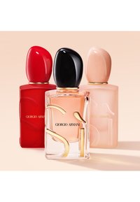 Tre Giorgio Armani Si parfymeflasker i rødt, klart og blek rosa med matchende skulpturerte hetter på beige bakgrunn.