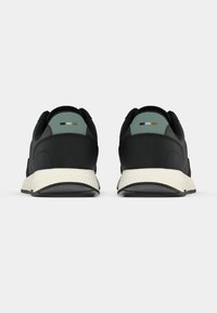 Ζευγάρι μαύρα αθλητικά παπούτσια με ανοιχτοπράσινες ταμπέλες στη φτέρνα και λευκές παχιές σόλες, να φαίνονται από πίσω σε λευκό φόντο.