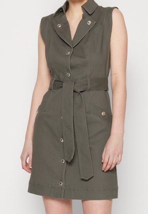 Vestido sin mangas de color verde oliva con cuello, botones delanteros, cinturón en la cintura y bolsillos con solapa abotonados, llevado por una persona de pie.