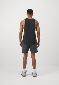 Ujjatlan fekete póló és szürke rövidnadrág. A pólónak lekerekített alja van, míg a rövidnadrág oldalhasítékokkal rendelkezik. A lábbelik szürke tornacipők.