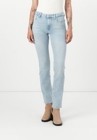 Jeans bleu clair en denim, coupe slim, design standard à cinq poches, avec fermeture éclair et bouton, associés à des bottines beiges à la cheville.