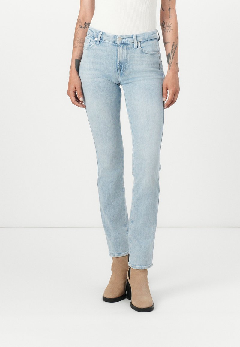 Jeans bleu clair en denim, coupe slim, design standard à cinq poches, avec fermeture éclair et bouton, associés à des bottines beiges à la cheville.