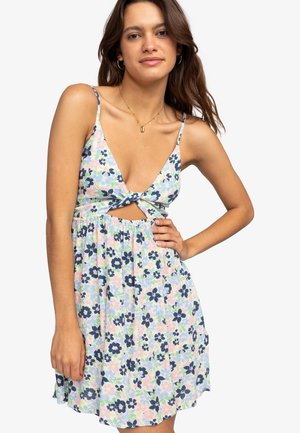 Vestido floral con escote en V y nudo en el frente, que presenta un fondo pastel con flores en tonos azul marino y verde. Tejido ligero y diseño sin mangas.
