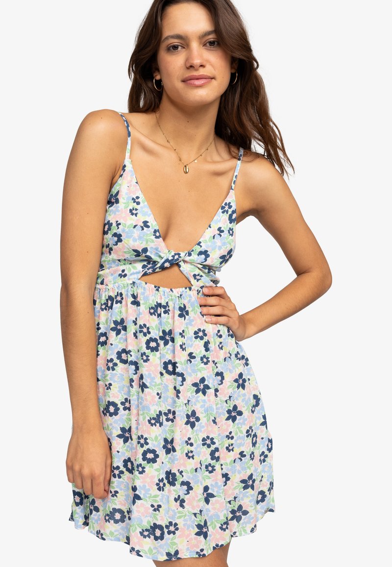 Blumenkleid mit V-Ausschnitt und Frontknot, ausgestattet mit einem pastellfarbenen Hintergrund und marineblauen sowie grünen Blumen. Leichter Stoff und ärmelloses Design.