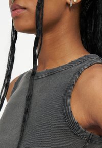 Κοντινό πλάνο ενός ατόμου που φοράει γκρι ριγωτό αμάνικο τοπ με μακριές μαύρες πλεξούδες που κρέμονται μπροστά από τον ώμο του.