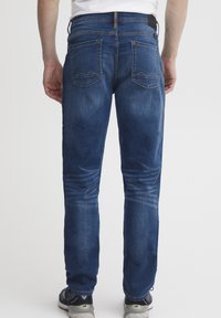 Jeans de mezclilla azul con un corte recto, que cuentan con dos bolsillos traseros con costuras visibles y una textura desgastada en las piernas.