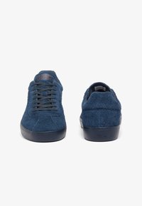 Zapatillas de ante azul marino con parte superior texturizada, cordones planos y suelas de goma; cuentan con un logo sutil en el talón y la lengüeta.