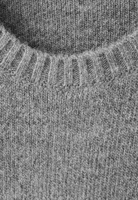 Dettaglio di un tessuto in lana grigia a maglia, con colletto a coste e un motivo a maglia testurizzato con fibre visibili.