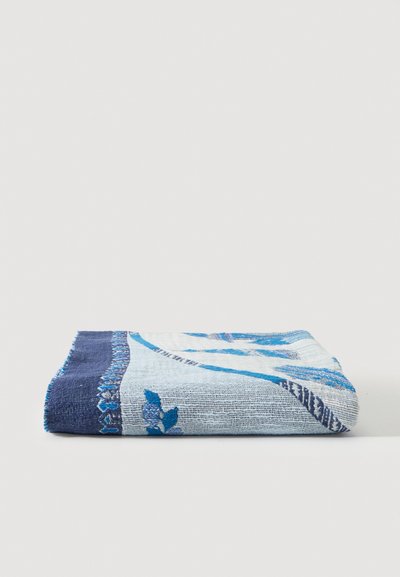 Serviette bleue et blanche pliée avec des motifs floraux et de feuilles placée sur une surface blanche plane.