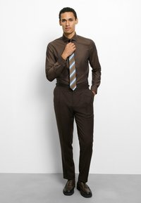 Braunes Hemd zum Knöpfen mit einem dezenten Muster, kombiniert mit dunkelbraunen Hosen und einer gestreiften Krawatte mit blauen und beigefarbenen Akzenten.