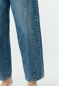 Hellblaue Jeans mit weitem Bein und entspannter Passform, versehen mit kontrastierenden Nähten und einem rohen Saum am Knöchel.